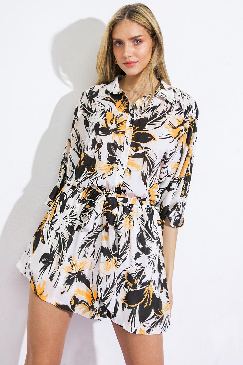 A printed woven romper featuring shirt collar, button down, dropped shoulder with kimono sleeve, elasticized waist with a self-sash tie
